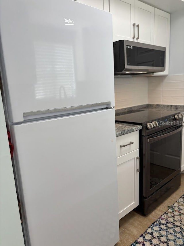 1055 6th Ave Unit A11, Vero Beach, FL 32960 - kitchen featuring freestanding refrigerator, stainless steel microwave, black electric range, backsplash, and white cabinetry