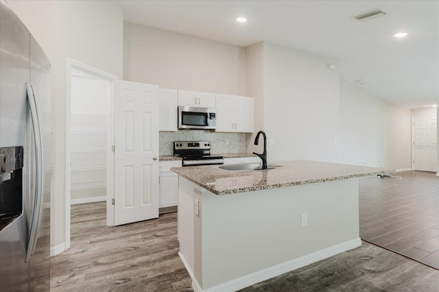 13016 Boggy Creek Dr, Riverview, FL 33579 - kitchen featuring appliances with stainless steel finishes, a sink, light wood-type flooring, light stone countertops, and white cabinetry