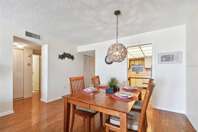 11000 Gulf Blvd Unit 703, Treasure Island, FL 33706 - dining room with light wood finished floors, a textured ceiling, a chandelier, and baseboards