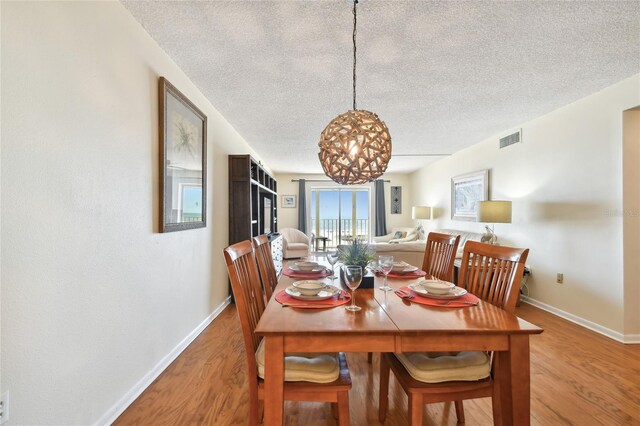 11000 Gulf Blvd Unit 703, Treasure Island, FL 33706 - dining space featuring a textured ceiling, light wood-type flooring, baseboards, and a chandelier