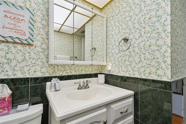 11000 Gulf Blvd Unit 703, Treasure Island, FL 33706 - bathroom featuring wallpapered walls, tile walls, toilet, vanity, and a wainscoted wall