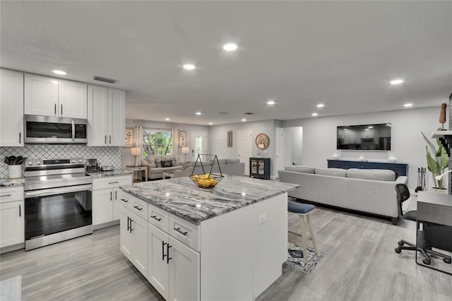 8222 Valrie Ln, Riverview, FL 33569 - kitchen with stainless steel appliances, open floor plan, a center island, white cabinetry, and light wood-style floors