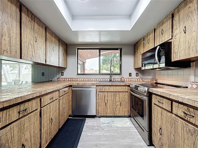 11525 Country Oaks Dr, Tampa, FL 33618 - kitchen featuring appliances with stainless steel finishes, a sink, a raised ceiling, backsplash, and light wood-style floors