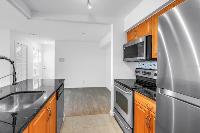 3305 Haviland Ct Unit 101, Palm Harbor, FL 34684 - kitchen featuring stainless steel appliances, brown cabinets, dark stone countertops, light tile patterned flooring, and backsplash