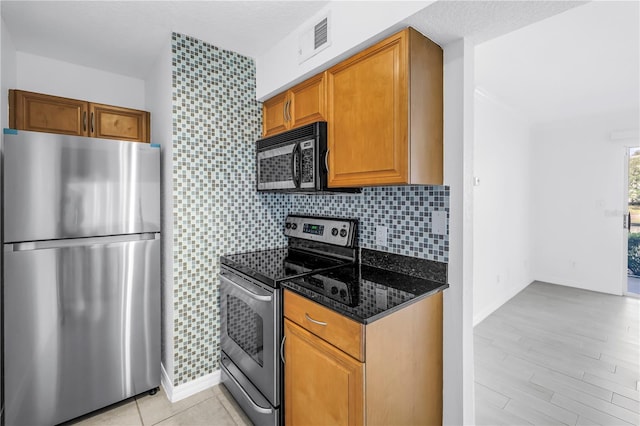 3300 Haviland Ct Unit 103, Palm Harbor, FL 34684 - kitchen with appliances with stainless steel finishes, dark stone counters, brown cabinetry, light wood-type flooring, and backsplash
