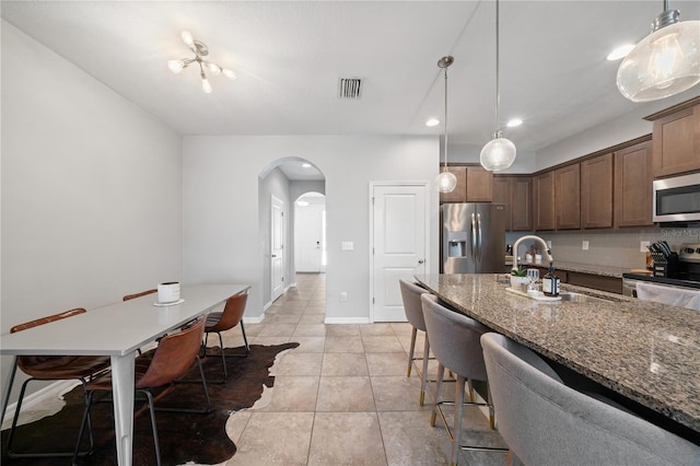 4504 Silver Lining St, Sarasota, FL 34238 - kitchen featuring stainless steel appliances, arched walkways, light tile patterned flooring, a breakfast bar, and dark stone countertops