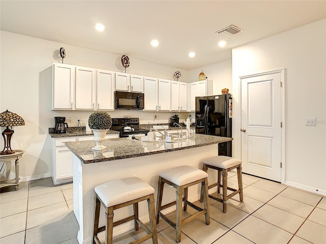 32977 Kaloko Rd, Wesley Chapel, FL 33543 - kitchen with black appliances, light tile patterned flooring, a breakfast bar area, dark stone counters, and white cabinetry