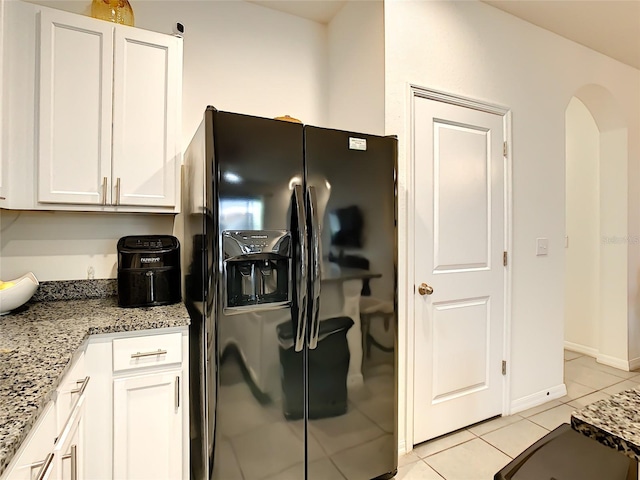 32977 Kaloko Rd, Wesley Chapel, FL 33543 - kitchen with black fridge, light tile patterned floors, white cabinetry, light stone countertops, and arched walkways