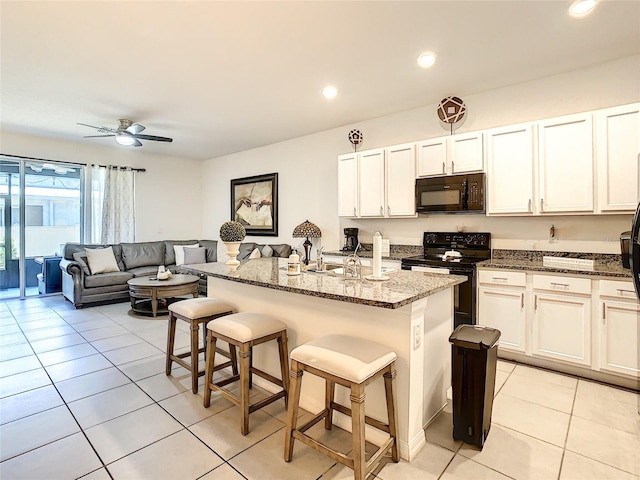 32977 Kaloko Rd, Wesley Chapel, FL 33543 - kitchen featuring black appliances, light tile patterned floors, a breakfast bar, dark stone countertops, and white cabinetry