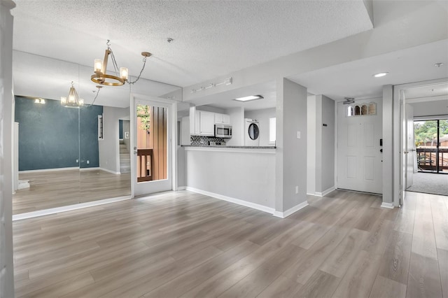 1038 E Michigan St Unit B, Orlando, FL 32806 - unfurnished living room featuring a chandelier, a textured ceiling, light wood-style flooring, baseboards, and stacked washer / drying machine