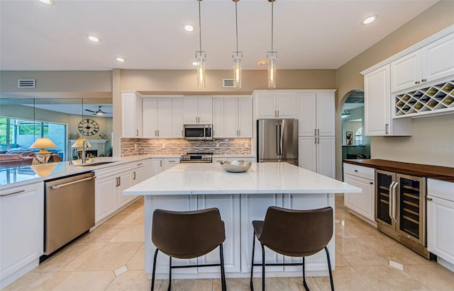 1710 Lago Vista Blvd, Palm Harbor, FL 34685 - kitchen featuring appliances with stainless steel finishes, wine cooler, backsplash, a kitchen island, and white cabinetry