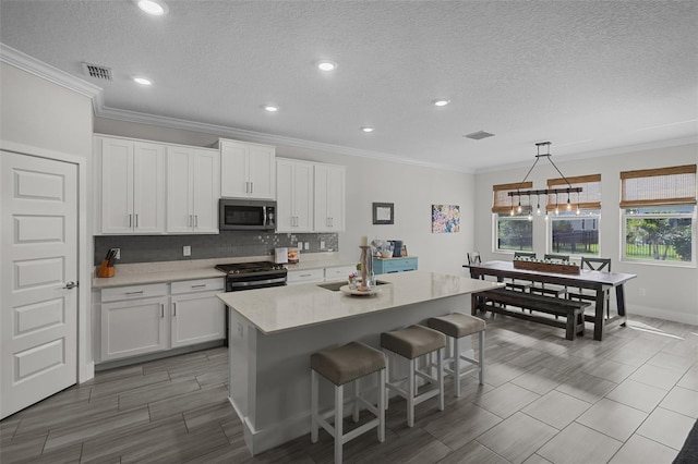 4077 Cadence Loop, Land O Lakes, FL 34638 - kitchen featuring appliances with stainless steel finishes, white cabinets, backsplash, a kitchen bar, and an island with sink