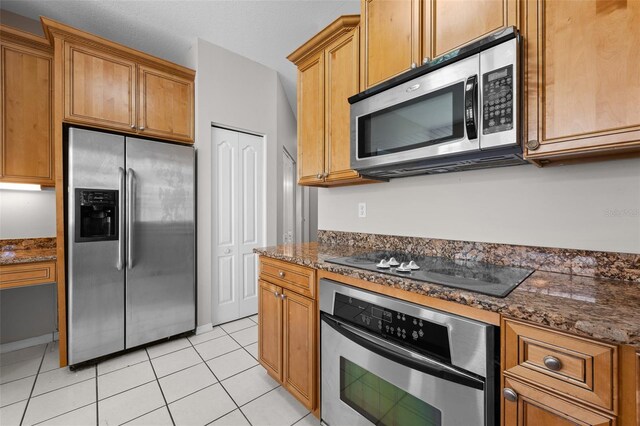 12209 Glencliff Cir, Tampa, FL 33626 - kitchen featuring appliances with stainless steel finishes, light tile patterned flooring, dark stone counters, and brown cabinets
