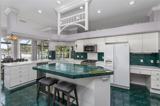 15012 Maurine Cove Ln, Odessa, FL 33556 - kitchen featuring stainless steel appliances, ornamental molding, a peninsula, decorative backsplash, and white cabinetry