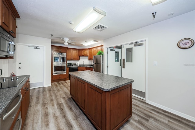 7932 Sailboat Key Blvd S Unit 406, South Pasadena, FL 33707 - kitchen with black appliances, dark countertops, light wood-type flooring, a kitchen island, and a ceiling fan