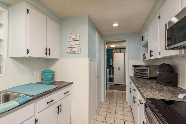 7901 Marlboro Dr, Port Richey, FL 34668 - kitchen featuring stainless steel microwave, dark countertops, white cabinetry, wainscoting, and a textured ceiling