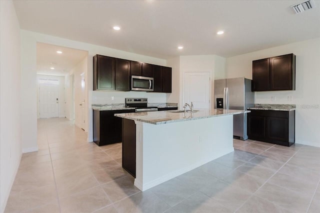 8210 Juning Cv, Wesley Chapel, FL 33545 - kitchen with appliances with stainless steel finishes, light stone countertops, a center island with sink, light tile patterned flooring, and recessed lighting