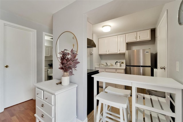 4215 E Bay Dr Unit 1801E, Clearwater, FL 33764 - kitchen with extractor fan, freestanding refrigerator, light countertops, white cabinetry, and a kitchen bar