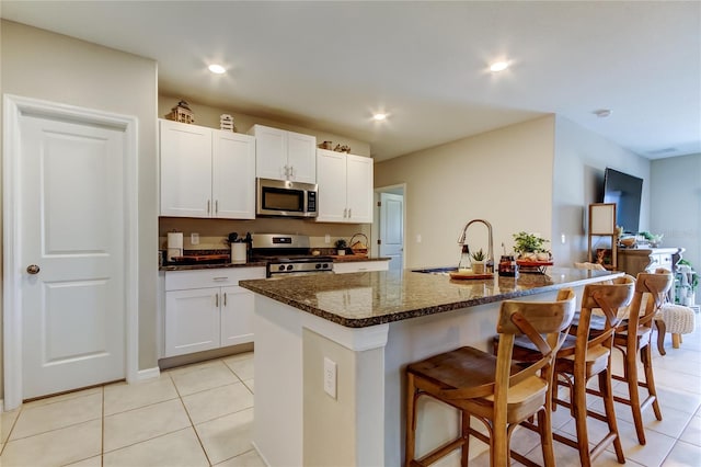 9334 Lemon Drop Loop, Sun City Center, FL 33573 - kitchen with appliances with stainless steel finishes, a sink, light tile patterned flooring, a kitchen bar, and dark stone countertops