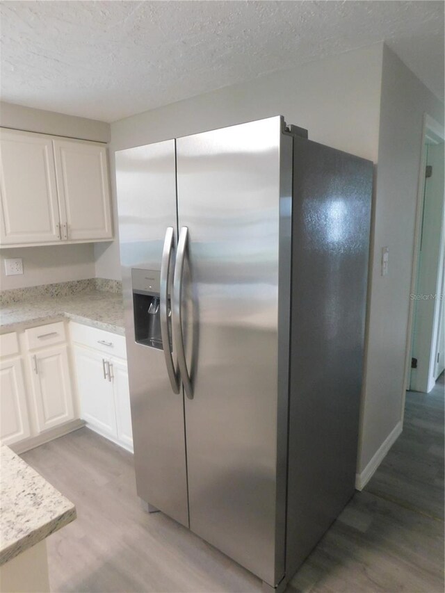 4417 Kohler St, New Port Richey, FL 34652 - kitchen featuring stainless steel fridge with ice dispenser, light wood-style floors, white cabinetry, a textured ceiling, and light stone counters