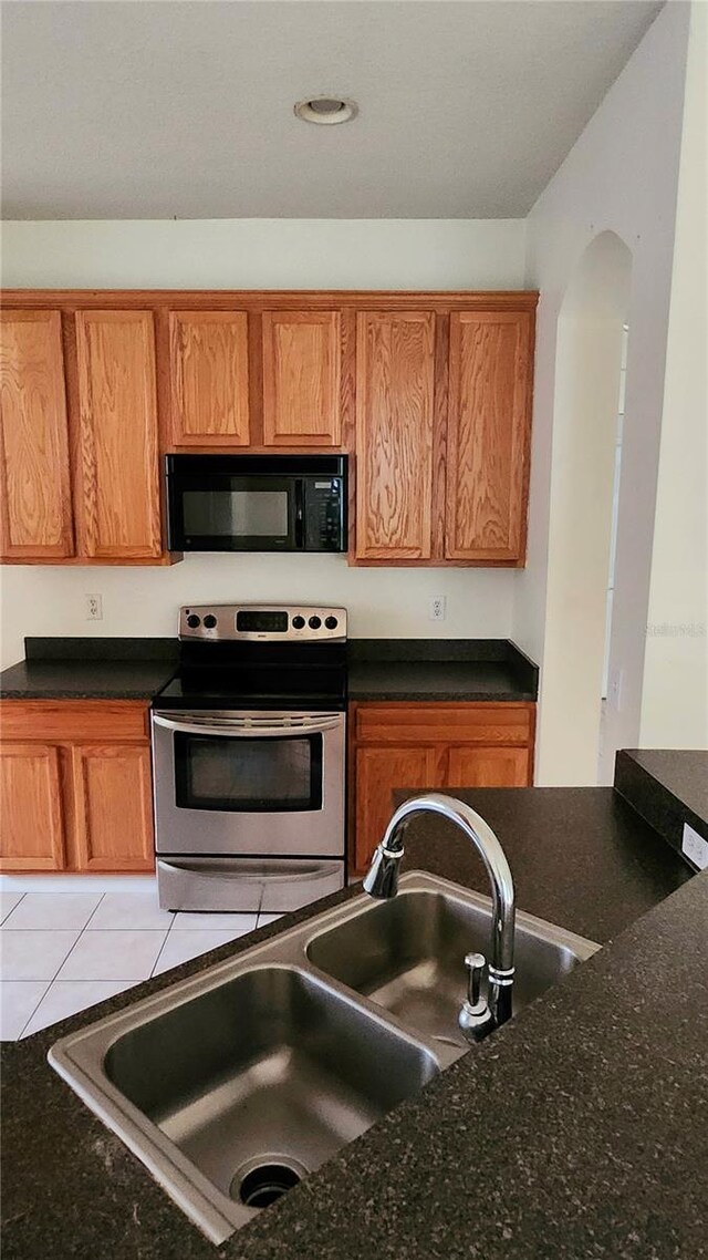 221 Fairmont Dr, Spring Hill, FL 34609 - kitchen featuring black microwave, stainless steel range with electric stovetop, brown cabinets, light tile patterned floors, and dark stone counters