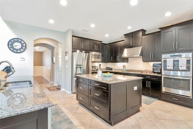 26972 Evergreen Chase Dr, Wesley Chapel, FL 33544 - kitchen featuring appliances with stainless steel finishes, under cabinet range hood, a center island, arched walkways, and light stone counters
