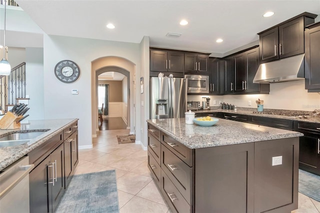 26972 Evergreen Chase Dr, Wesley Chapel, FL 33544 - kitchen featuring under cabinet range hood, appliances with stainless steel finishes, arched walkways, a kitchen island, and light tile patterned floors