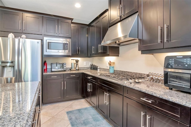 26972 Evergreen Chase Dr, Wesley Chapel, FL 33544 - kitchen featuring under cabinet range hood, appliances with stainless steel finishes, light tile patterned floors, light stone countertops, and dark brown cabinetry