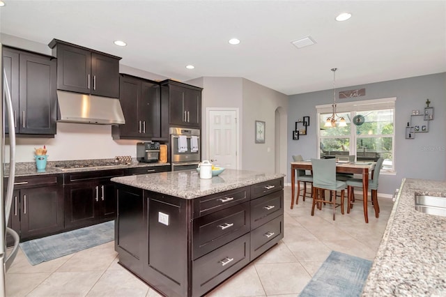 26972 Evergreen Chase Dr, Wesley Chapel, FL 33544 - kitchen with under cabinet range hood, stainless steel appliances, arched walkways, light tile patterned flooring, and a center island