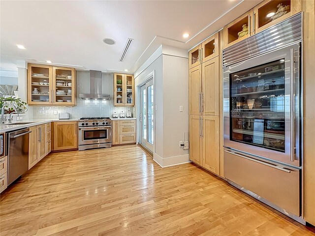 301 23rd Ave NE, Saint Petersburg, FL 33704 - kitchen featuring high quality appliances, wall chimney exhaust hood, light wood-style flooring, glass insert cabinets, and tasteful backsplash