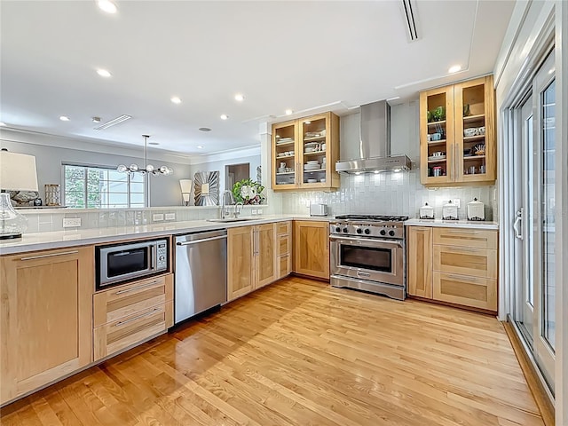 301 23rd Ave NE, Saint Petersburg, FL 33704 - kitchen with stainless steel appliances, wall chimney range hood, light brown cabinetry, light wood-style floors, and backsplash