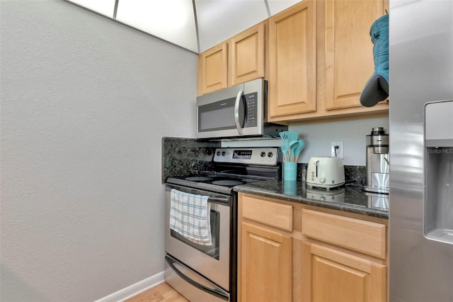 14130 Rosemary Ln Unit 3202, Largo, FL 33774 - kitchen with appliances with stainless steel finishes, light brown cabinets, a textured wall, dark stone counters, and light wood finished floors