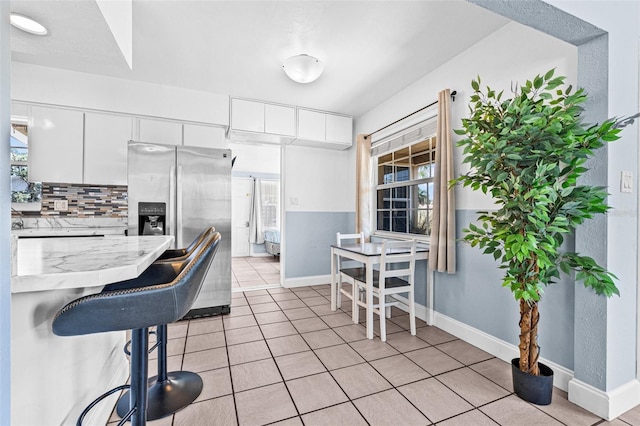 2861 Pinellas Point Dr S, Saint Petersburg, FL 33712 - kitchen featuring stainless steel fridge, baseboards, white cabinets, light tile patterned floors, and a breakfast bar