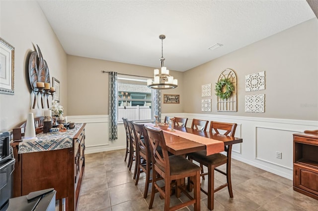 4151 Little Gap Loop, Ellenton, FL 34222 - dining space featuring a chandelier, a decorative wall, light tile patterned floors, a wainscoted wall, and a textured ceiling