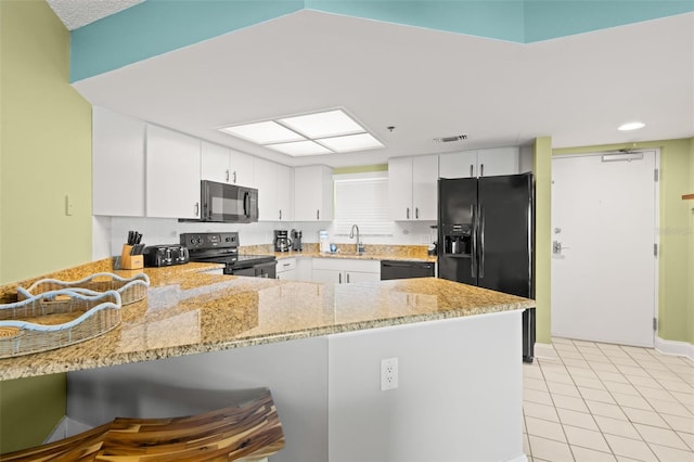 4510 Gulf Blvd Unit 604, St Pete Beach, FL 33706 - kitchen with black appliances, a peninsula, light stone countertops, white cabinetry, and light tile patterned flooring