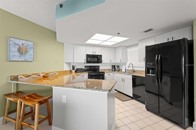 4510 Gulf Blvd Unit 604, St Pete Beach, FL 33706 - kitchen featuring black appliances, a peninsula, light stone countertops, and white cabinetry