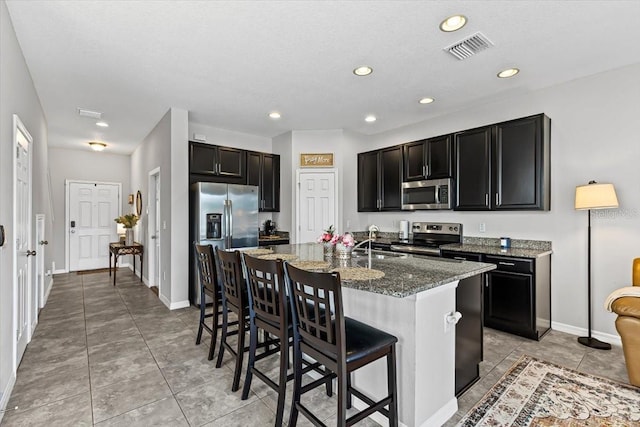 7916 Evergreen Creek Ct, Riverview, FL 33578 - kitchen with stainless steel appliances, dark cabinets, a kitchen bar, dark stone countertops, and an island with sink