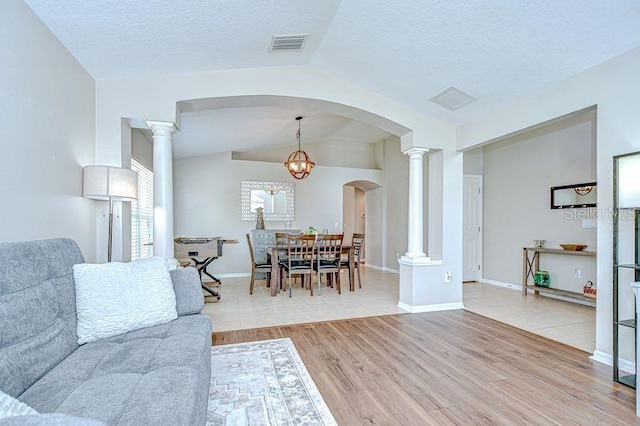 31349 Philmar Ln, Wesley Chapel, FL 33543 - living area featuring lofted ceiling, ornate columns, arched walkways, light wood-style flooring, and a textured ceiling