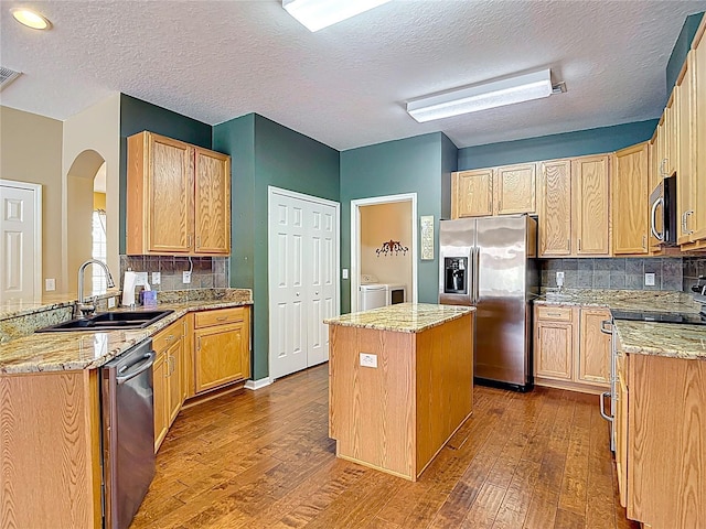 3824 Duke Firth St, Land O Lakes, FL 34638 - kitchen featuring appliances with stainless steel finishes, washer and clothes dryer, dark wood-style flooring, a center island, and backsplash