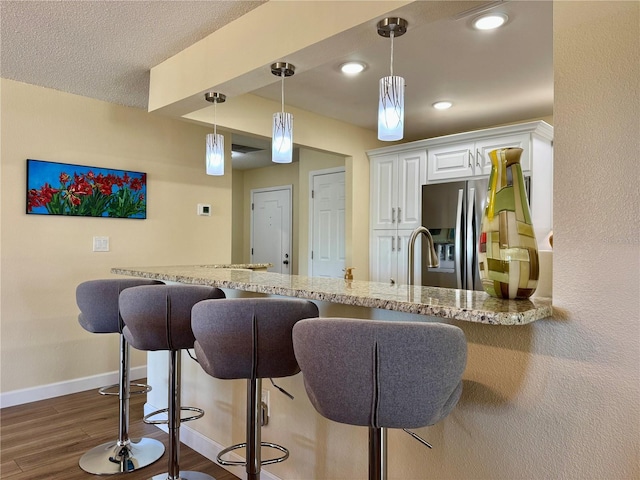100 Bluff View Dr Unit 115C, Belleair Bluffs, FL 33770 - kitchen with stainless steel refrigerator with ice dispenser, light stone counters, a breakfast bar area, dark wood-style flooring, and white cabinetry