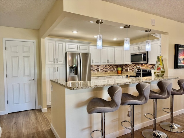 100 Bluff View Dr Unit 115C, Belleair Bluffs, FL 33770 - kitchen with stainless steel appliances, white cabinets, a kitchen bar, light stone counters, and a textured ceiling