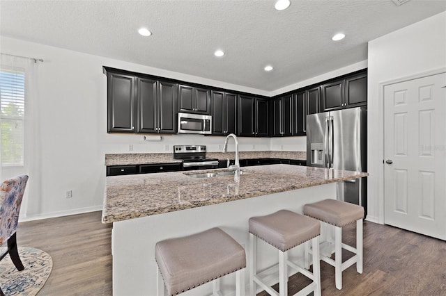 11434 Leland Groves Dr, Riverview, FL 33579 - kitchen with stainless steel appliances, dark cabinetry, a breakfast bar area, light stone countertops, and wood finished floors
