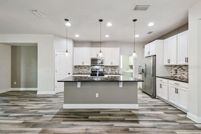 1553 Amber Leaf Cir, Ocoee, FL 34761 - kitchen featuring stainless steel appliances, wood finished floors, decorative backsplash, an island with sink, and white cabinetry