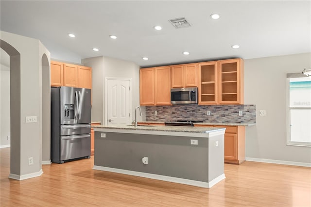 826 Addison Dr NE, Saint Petersburg, FL 33716 - kitchen featuring appliances with stainless steel finishes, arched walkways, light wood-style floors, tasteful backsplash, and a kitchen island with sink