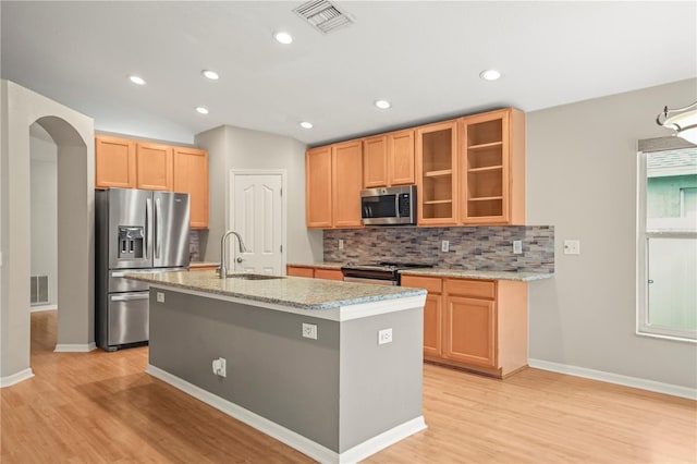 826 Addison Dr NE, Saint Petersburg, FL 33716 - kitchen with appliances with stainless steel finishes, light wood-type flooring, decorative backsplash, a center island with sink, and glass insert cabinets