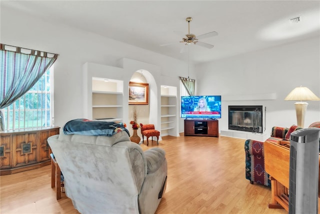 22946 Brownwood Ct, Land O Lakes, FL 34639 - living room featuring ceiling fan, light wood-style flooring, built in features, and a glass covered fireplace