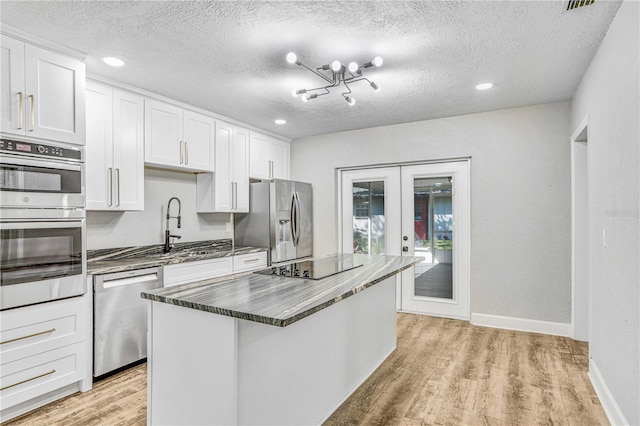 223 Pinehurst Dr, Auburndale, FL 33823 - kitchen with stainless steel appliances, french doors, light wood-style floors, white cabinets, and a center island