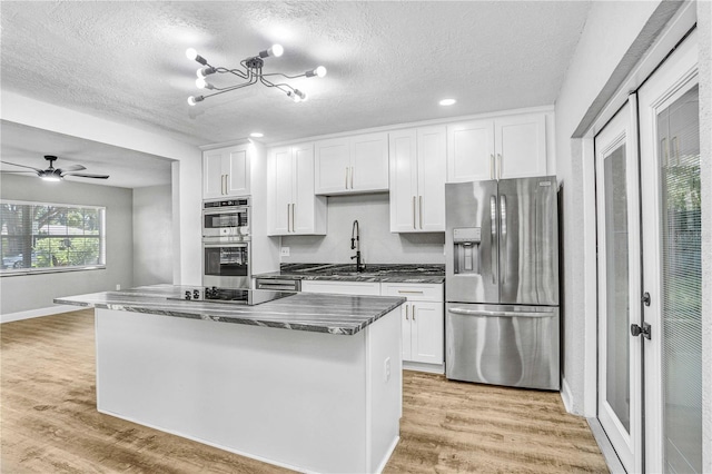 223 Pinehurst Dr, Auburndale, FL 33823 - kitchen with stainless steel appliances, white cabinets, light wood-type flooring, a kitchen island, and a textured ceiling