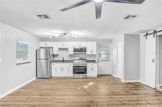 223 Pinehurst Dr, Auburndale, FL 33823 - kitchen with appliances with stainless steel finishes, a barn door, white cabinets, light wood-type flooring, and a textured ceiling