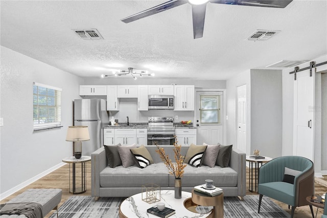 223 Pinehurst Dr, Auburndale, FL 33823 - living room with a barn door, light wood-style flooring, a ceiling fan, and a textured ceiling